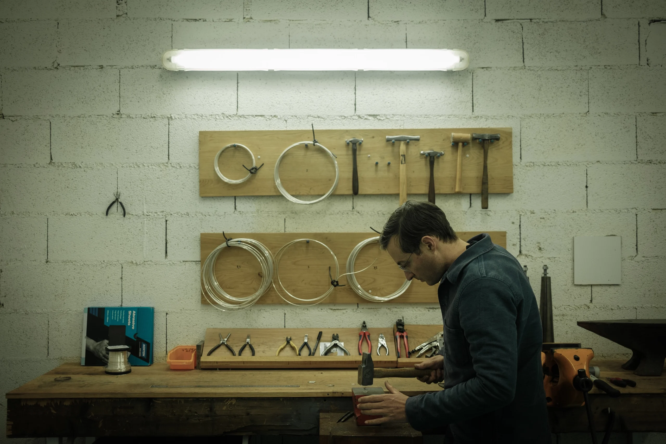Adrien Moniquet en train de marteler une tige métallique à l’établi dans son atelier