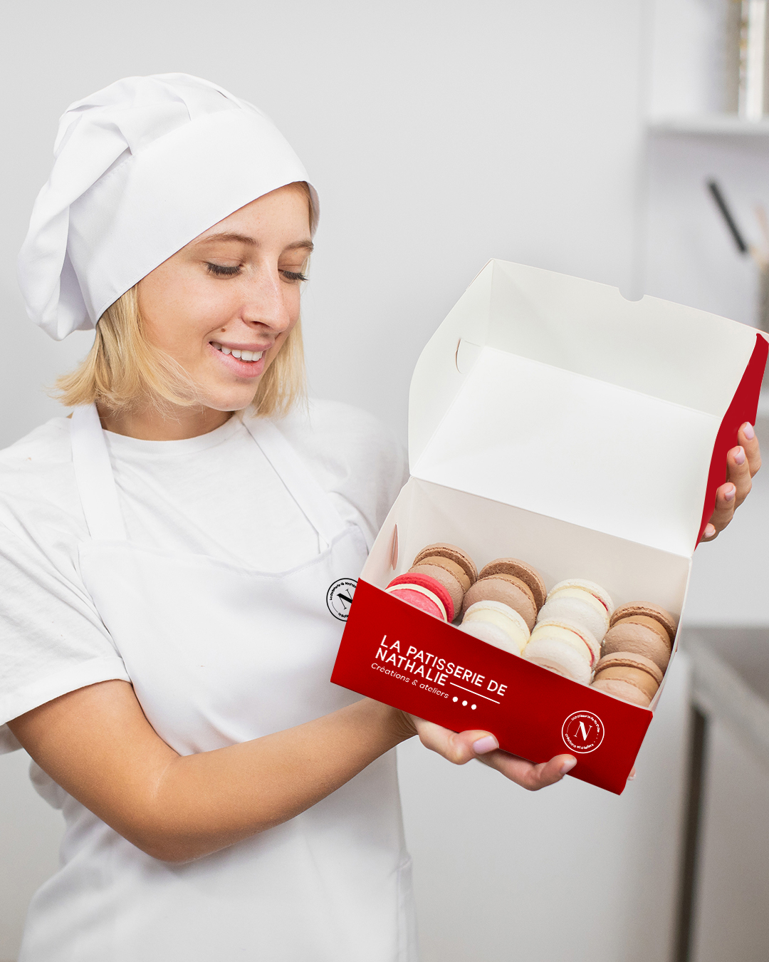 Pâtissière souriante plaçant des macarons dans un coffret rouge signé La Pâtisserie de Nathalie