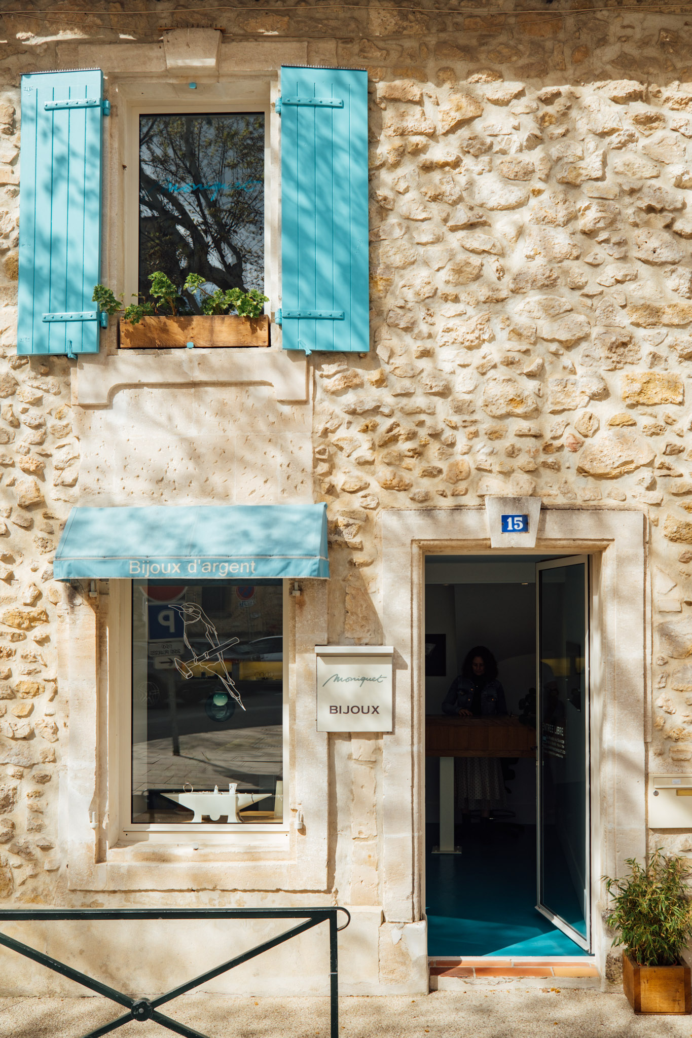 Entrée de la boutique Adrien Moniquet à Maussane-les-Alpilles avec façade en pierre et auvent bleu