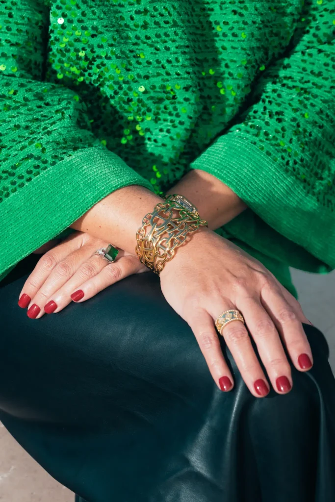 Détails mode lookbook : pull vert à sequins, bijoux dorés et manucure rouge, ambiance fashion La Joliette.