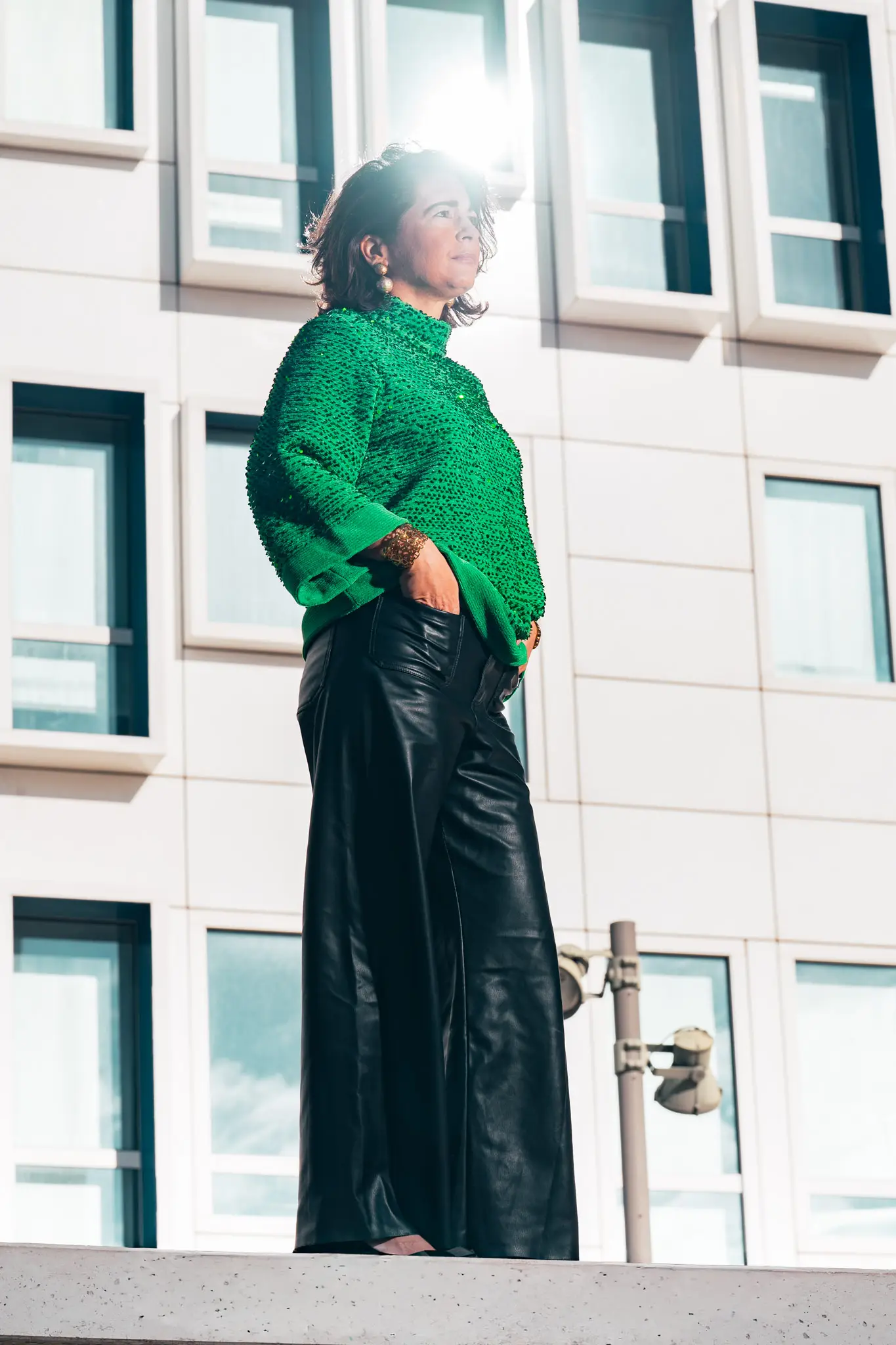Portrait lookbook mode : pull vert à sequins et pantalon cuir noir, contre façade moderne à La Joliette.
