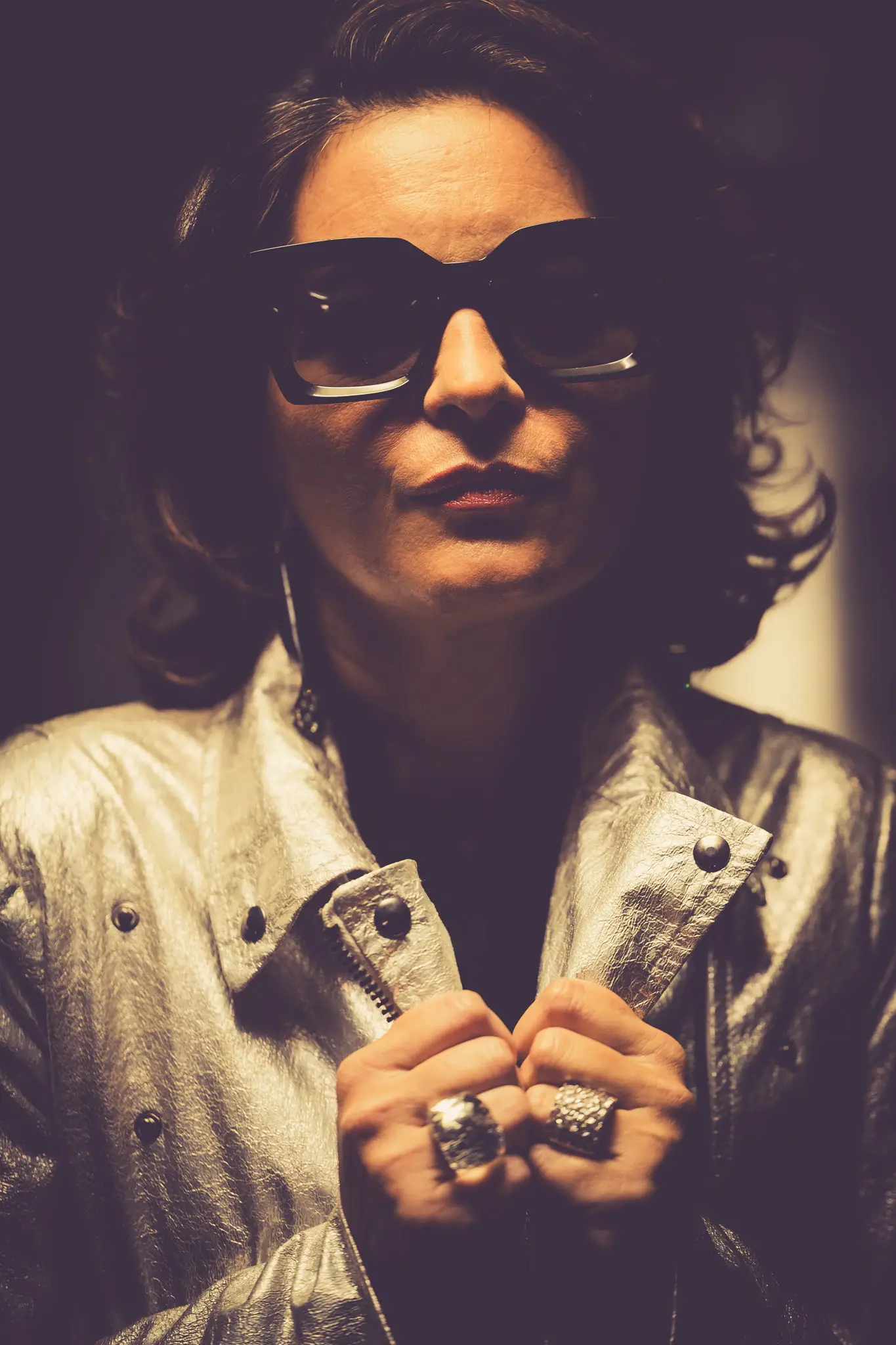 Portrait fashion rétro futuriste avec veste métallisée argent et lunettes oversize dans une lumière dramatique.