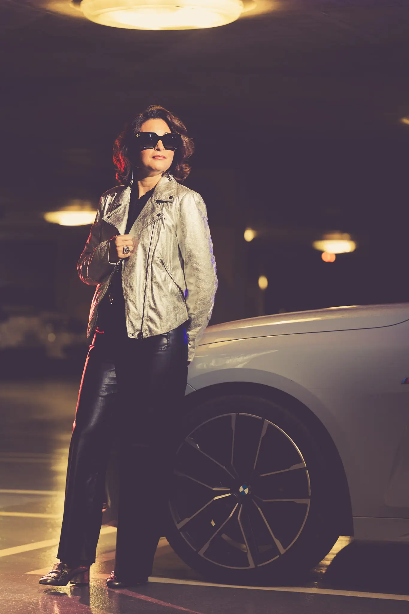 Silhouette fashion en veste métallisée argent et lunettes oversize dans un parking urbain.