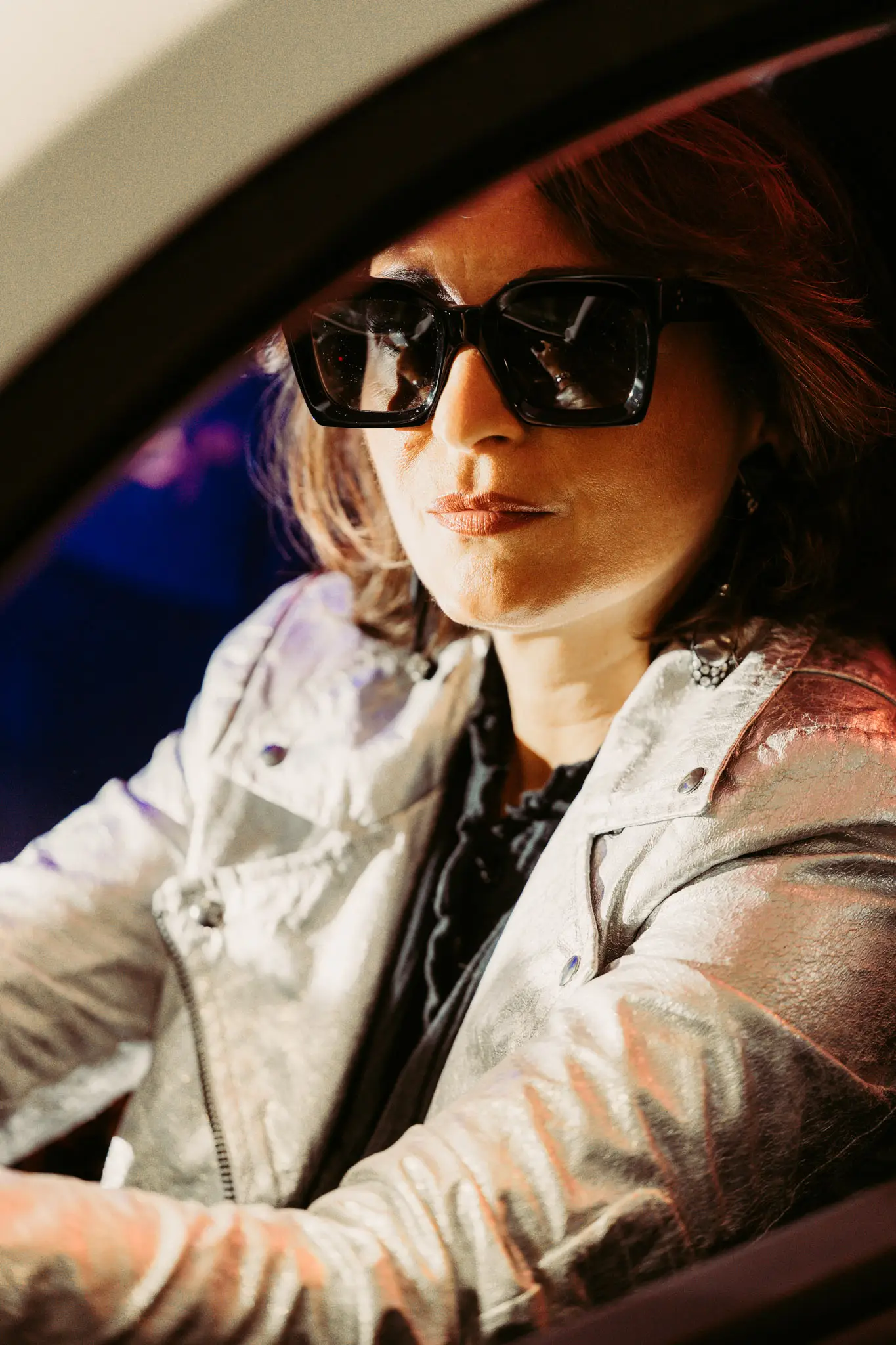 Portrait fashion rétro futuriste en veste argent et lunettes oversize dans une voiture.