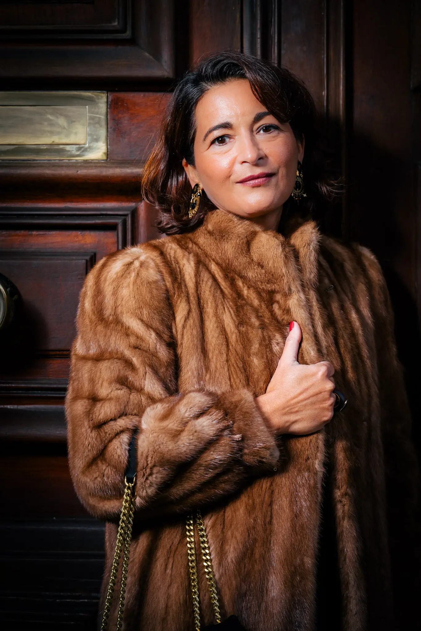 Silhouette chic en manteau de fourrure devant une porte en bois sombre pour un lookbook fashion inspiré Yves Saint Laurent.