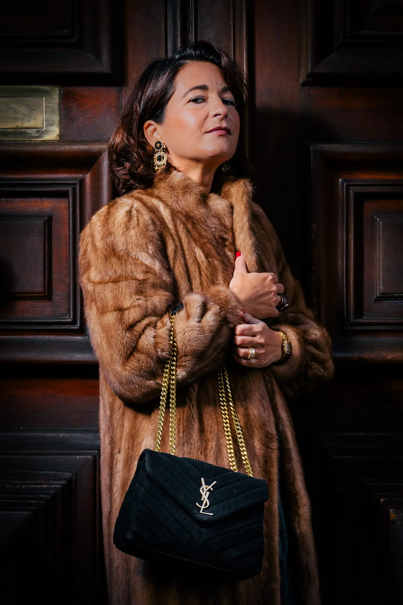 Silhouette chic en manteau de fourrure avec sac YSL devant une porte en bois sombre pour un lookbook fashion haut de gamme.